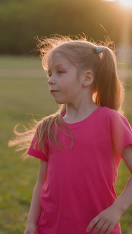 cute girl with injured eye shakes ponytails on lush field at sunset time slow motion. active playing in summer park. pretty hairstyle and game