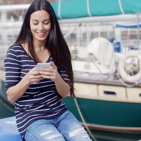 mujer joven sentada en un muelle revisando su móvil