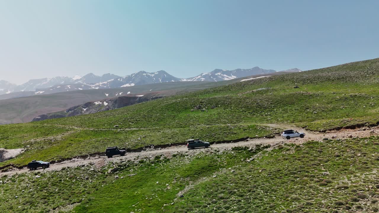Cars drive through hilly landscape under clear sky, adventurous travel