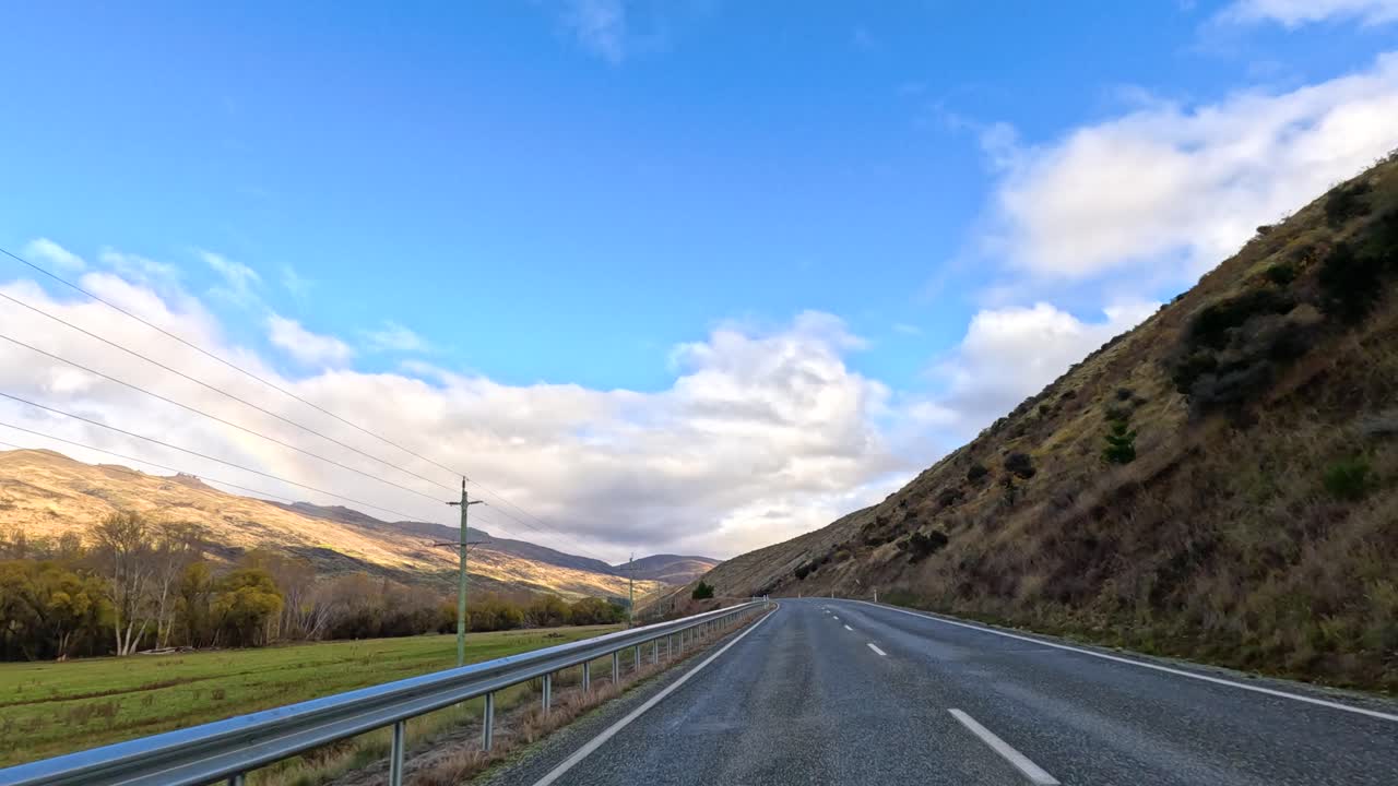 A serene drive through Wanaka's picturesque roads, capturing rolling hills and vibrant skies under natural daylight