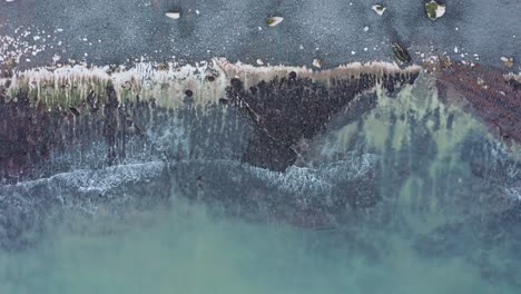 Descending-top-down-aerial-shot-of-blue-water-waves-crashing-on-wild-rugged-beach