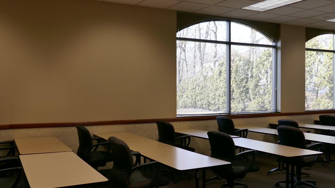 Bright windows in empty classroom with tables and chairs