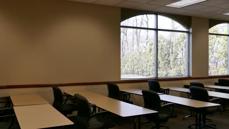 bright windows in empty classroom with tables and chairs