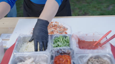 pizza maker adding toppings to pizza outdoors in slow motion