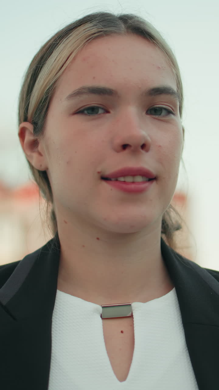 Nærbillede af en hvid kvinde, der står selvsikkert udendørs i moderne omgivelser med hænderne i taljen og udstråler ro og selvtillid med sløret udsigt til folk, der går i baggrunden.