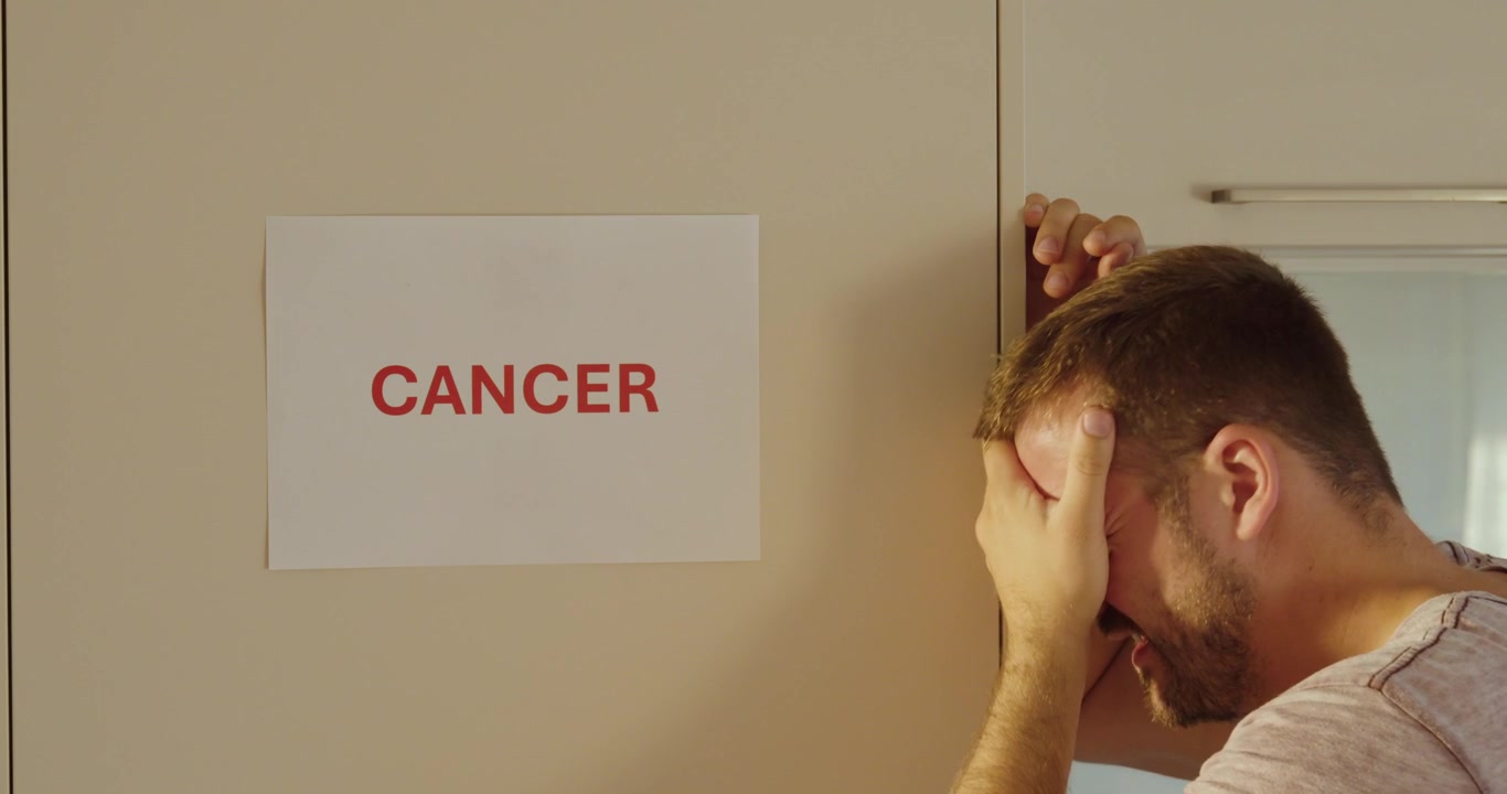 Uomo che piange e scuote la testa in preda alla disperazione dopo la notizia del cancro, rappresentando la lotta emotiva, la malattia e le sfide per la salute.