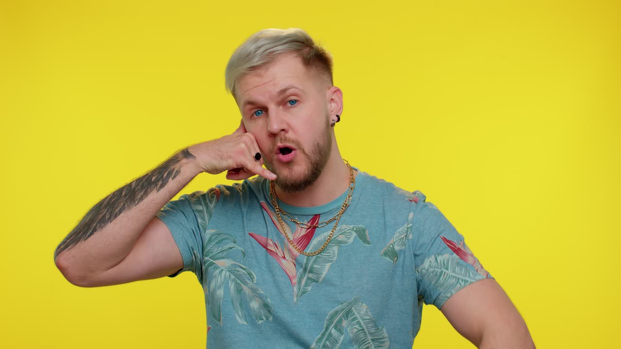 Glad mand i t-shirt, der ser på kameraet og laver en telefonbevægelse, som om han siger hej, du ringer mig tilbage