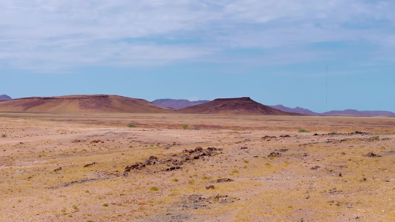 Vista aérea de una mesa de cima plana elevándose sobre las llanuras secas de Damaraland en el noroeste de Namibia. Árboles dispersos y hierba seca se extienden por las vastas llanuras áridas hacia distantes montañas de mesa azules.
