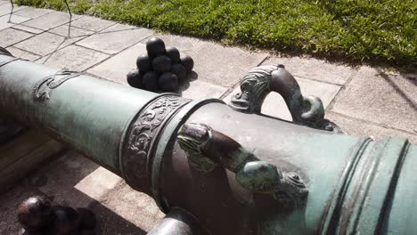 Closeup-panning-length-of-antique-cannon-length-with-stacks-of-cannonballs