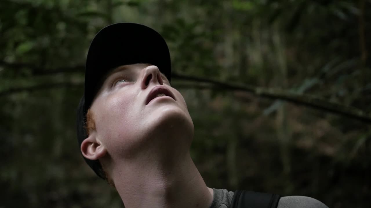 Nærbillede af ung, nysgerrig, kaukasisk mand med hat, der kigger op i den brasilianske regnskov og udforsker området i slowmotion.