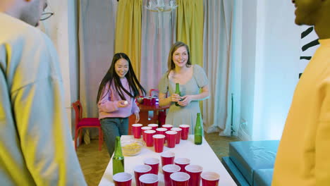 happy multiethnic young friends playing beer pong at home