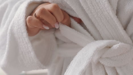 Woman-ties-belt-of-soft-bathrobe-spending-time-at-spa-resort