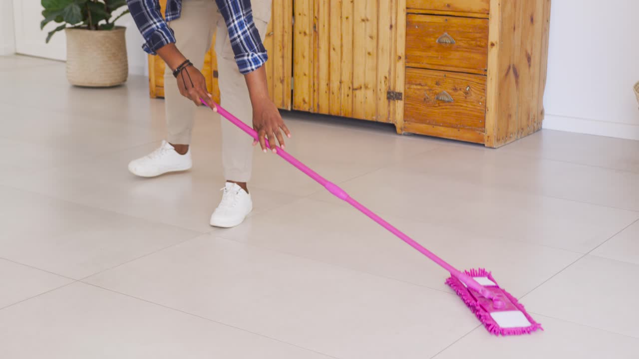 Afroamerikansk mann starter med en rosa mopp, mopper stuegulvet rundt en blå sprayflaske