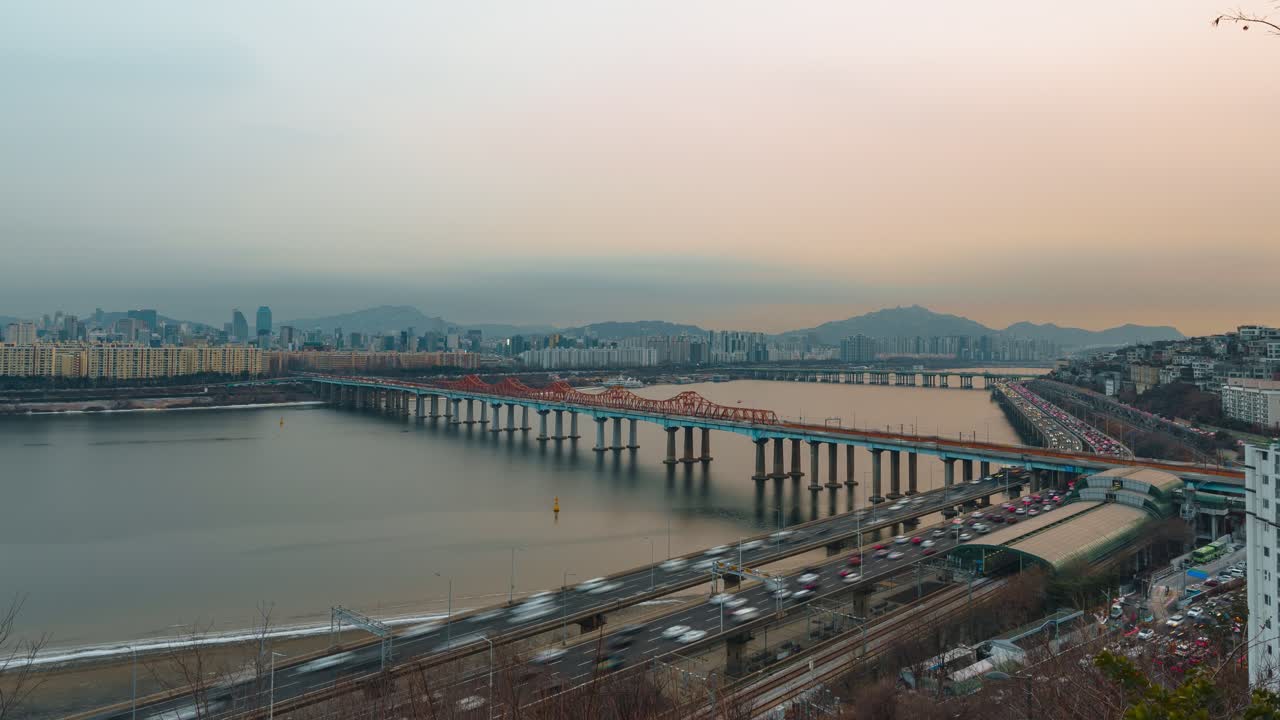 Seul, Corea del Sud — hyperlapse panoramico, traffico intenso sull'autostrada Gangbyeonbuk-ro, Ponte Donho che attraversa il fiume Han, skyline residenziale, montagne, tramonto invernale caldo e velato
