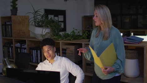 caucasian woman and biracial man collaborate on a business project in an office, working late