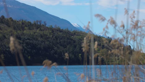 Idílica-Panorámica-En-Cámara-Lenta-De-La-Vista-Del-Paisaje-De-Impresionantes-Colinas-Y-Montañas-Cubiertas-De-Bosques-Junto-A-Las-Tranquilas-Aguas-Del-Lago-Toblino,-Italia