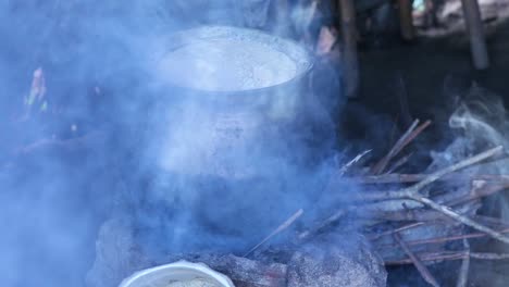 a large pot of food cooks on a typical stove fueled by sticks in a rural asian home