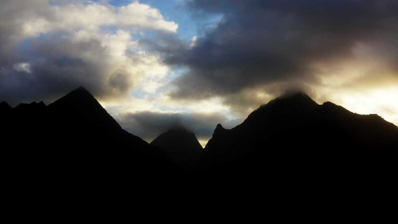 Vue aérienne par drone des sommets des montagnes de Teahupoo en silhouette à l'heure dorée, Tahiti, avec des nuages de coucher de soleil spectaculaires rougeoyant d'orange derrière la crête sombre.