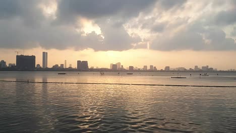 Ein-Erstaunlicher-Blick-Auf-Den-Sonnenuntergang-Und-Die-Treibenden-Wolken-über-Dem-Wasser-Mit-Der-Stadt-Im-Hintergrund