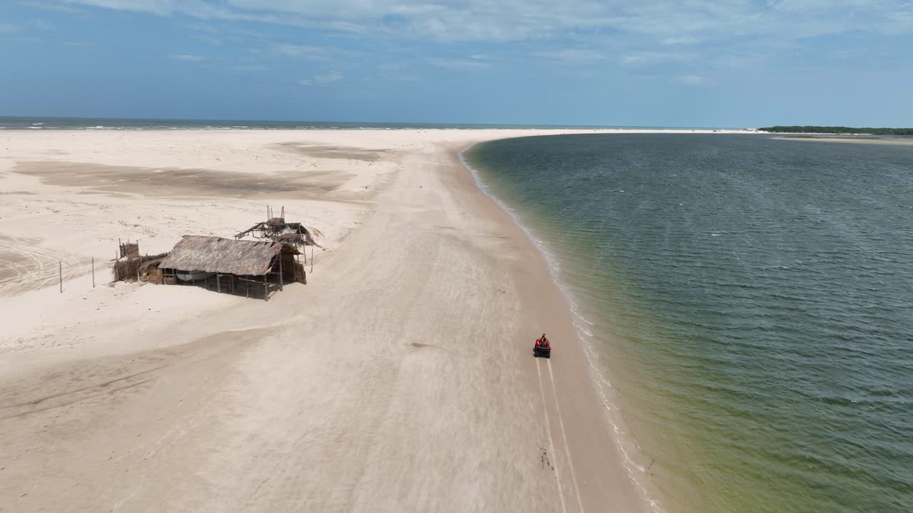 Aerial of white sand beach and river outlet where Parnaiba River meets the sea as off road vehicle races along shore