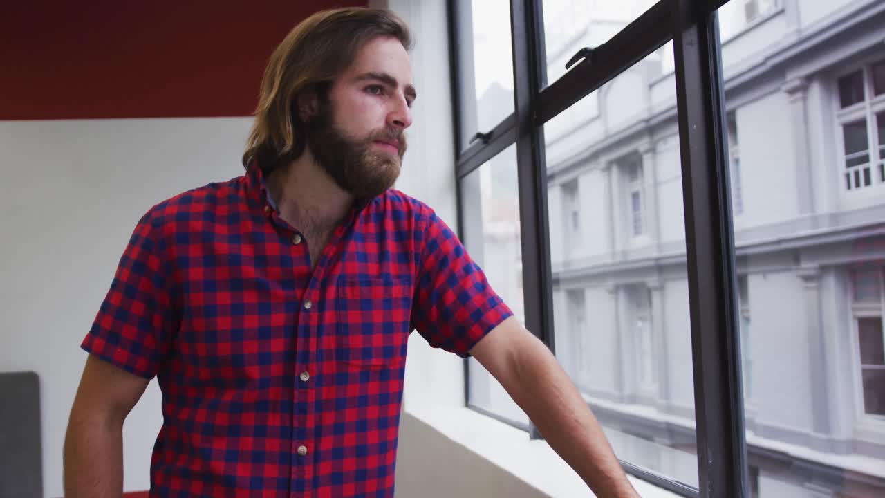 hombre de negocios caucásico de pie mirando por la ventana en una oficina moderna