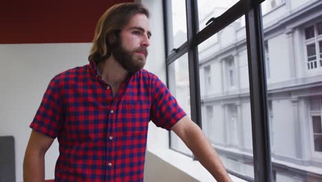 caucasian businessman standing looking out of window in modern office