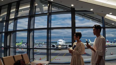 wide-angle shot of two people at an airport terminal, observing planes through large windows