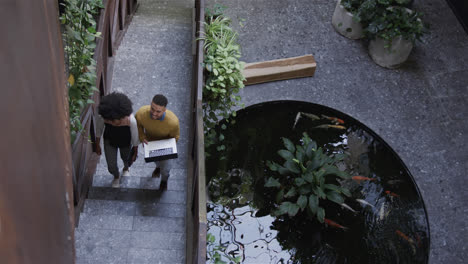 diverse male and female colleague walking up stairs using laptop, talking, copy space, slow motion