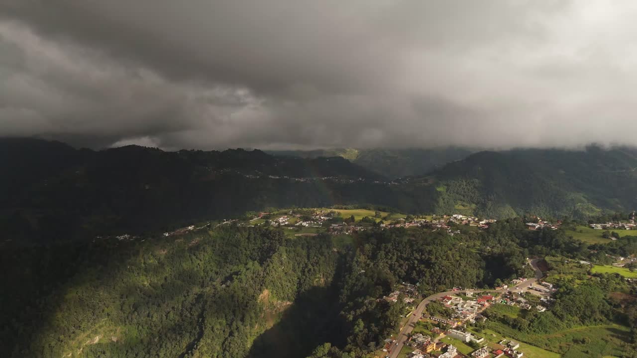 Forward drone flight over Zacatlán Valley, showing cloud shadows, sun rays breaking through, green mountains and scattered houses in the landscape