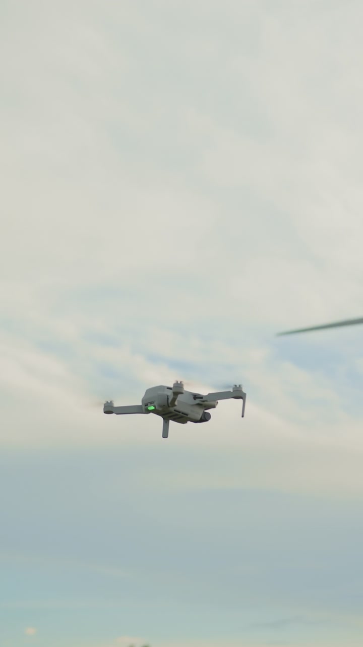 Piccolo drone con eliche che girano si libra su uno sfondo di nuvole soffici e diffuse e un pallido.