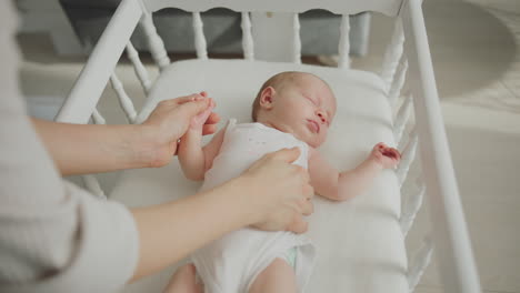 mother gently holding and caring for newborn baby in a white crib