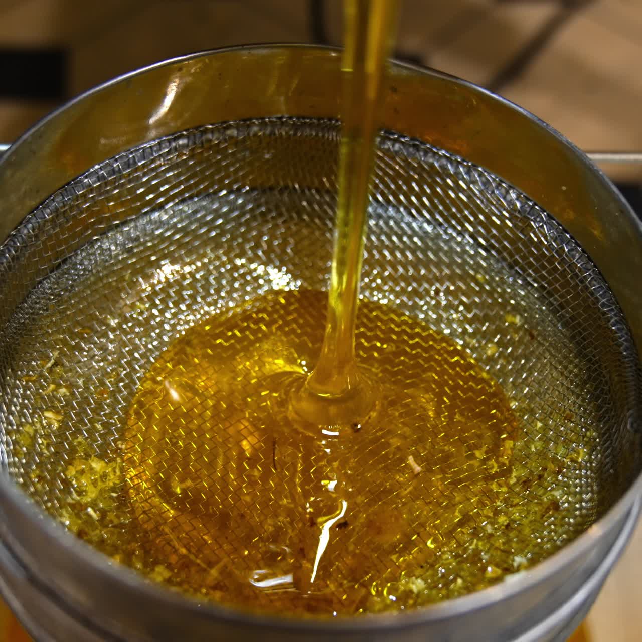 Metal sieve on top of the bucket for honey filtering. Fresh yellow liquid honey starts to flow from the machine. Healthy organic food concept