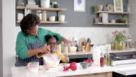 happy african american mother and daughter preparing dough in bowl in kitchen, slow motion