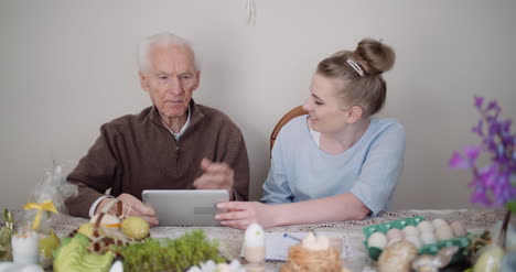 old man retirement smiling senior man talking with granddaughter while using digital tablet 1