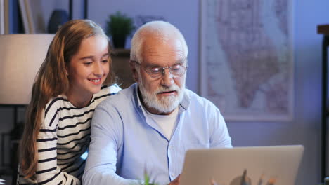 Smiled-Grandfather-And-Granddaughter-Sitting-Being-In-The-Cabinet-At-Home-And-Having-A-Videochat-On-The-Laptop-Computer-Late-At-Night