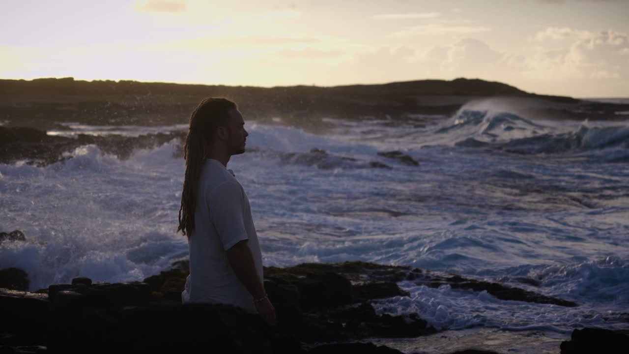 Un momento di tranquillità: un uomo seduto di fronte al mare, circondato da rocce frastagliate e dal suono delle onde che si infrangono, che riflette pace, meditazione e unione con il flusso della natura