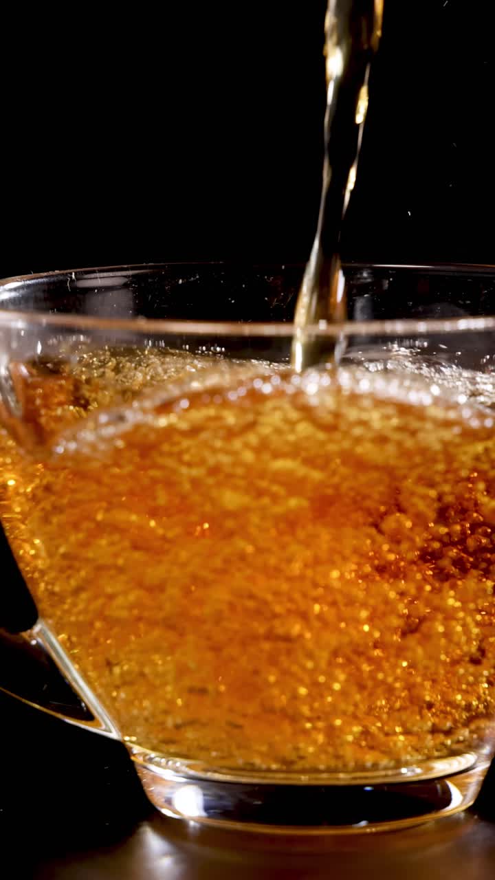 Il tè viene versato in una tazza di vetro trasparente su uno sfondo scuro, evidenziando il colore intenso e le bollicine del liquido.