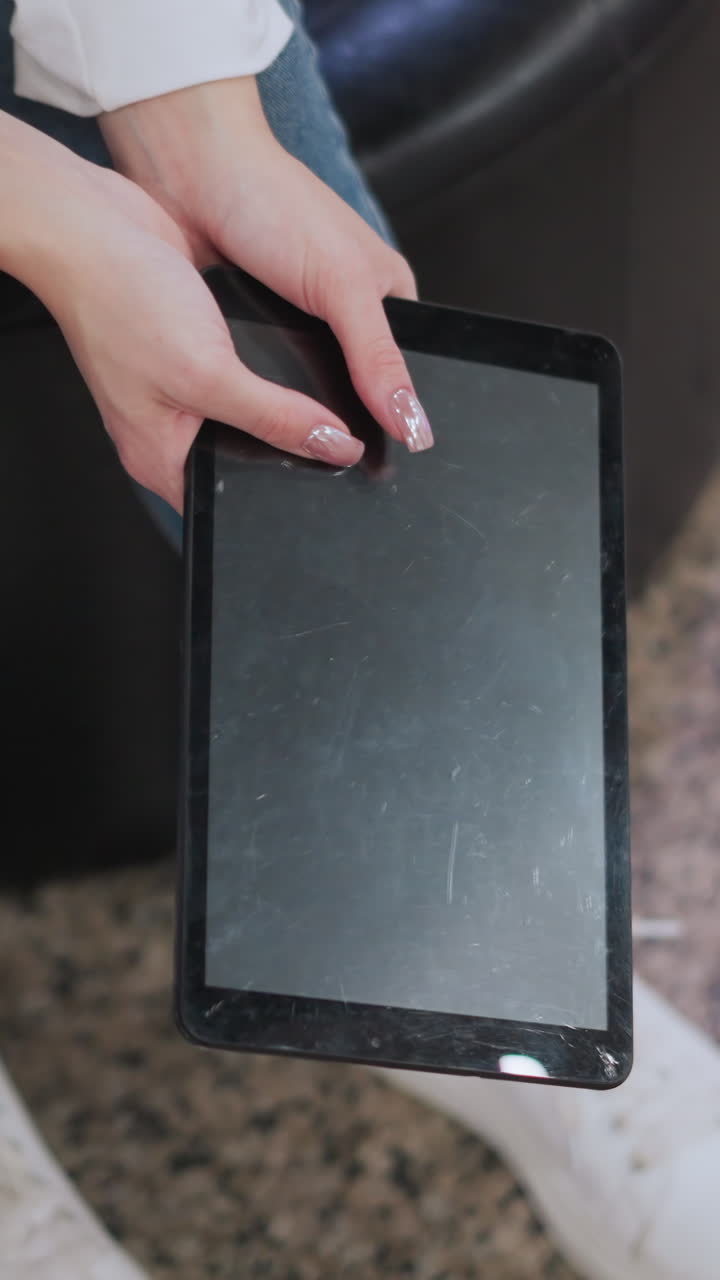 manos sosteniendo una tableta, inclinándola suavemente con reflejos suaves en la pantalla, traje casual con vaqueros de denim y zapatillas blancas hace hincapié en el estilo de vida moderno en iluminación sutil y pisos reflectantes