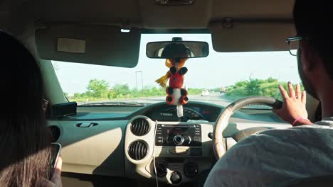 View-Behind-A-Couple-Riding-And-Driving-A-Car-On-The-Asphalt-Road-In-Agra,-India---close-up