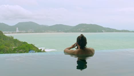 medium close of a pretty young woman in a private swimming pool and relaxing by taking a selfie with the viewpoint and open space