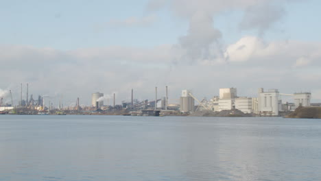 wide shot of polluting industrial buildings standing on river shore