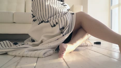 closeup barefoot girl covered with soft plaid sits on floor