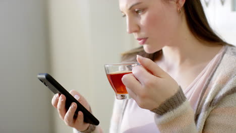 caucasian woman using smartphone and drinking tea at home, in slow motion