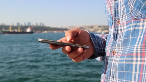 hombre usando teléfono móvil en el fondo vista del mar de cerca manos 1