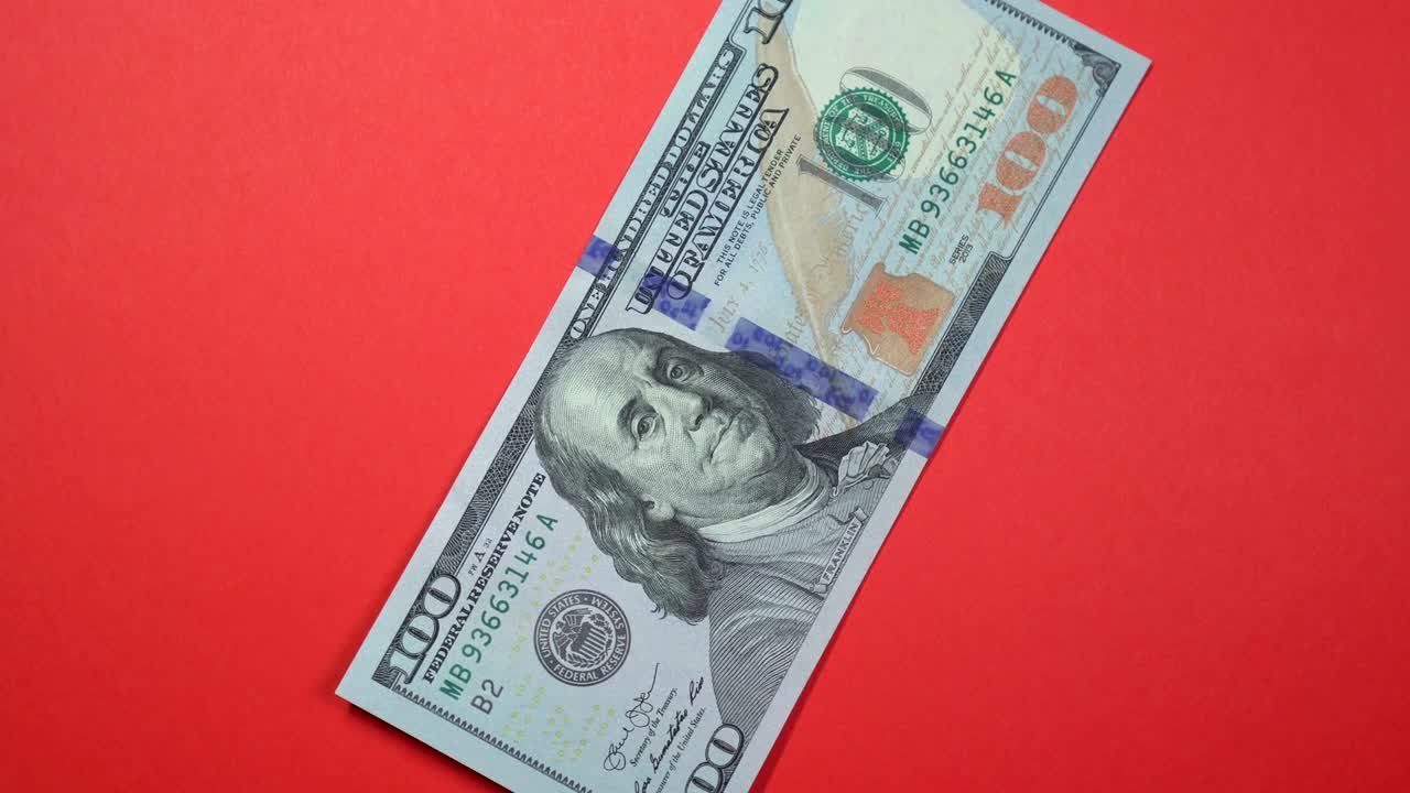 One hundred dollars slowly spinning on a rotating red background.