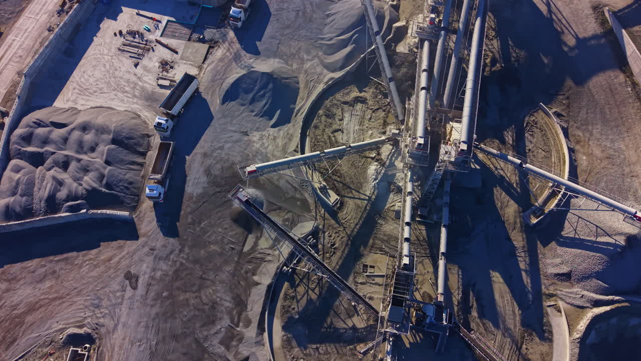 Aerial view of a busy construction site showcasing intricate machinery and vast piles of gravel under a clear blue sky
