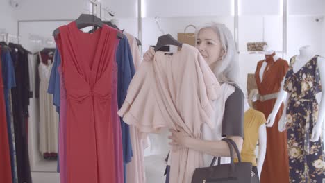 cheerful female shopper picking dress with hanger from rack and looking at herself on the mirror