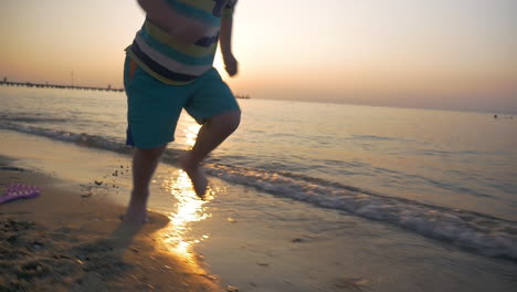 niño corriendo descalzo a lo largo del mar al atardecer
