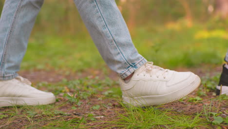 vista de cerca lateral de excursionistas caminando por un sendero forestal, uno con zapatillas blancas y vaqueros azules, el otro con zapatillas negras