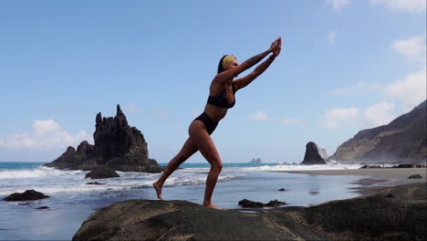 con un ritmo suave, una mujer joven, delgada y elegante, practica yoga en una roca costera en cámara lenta